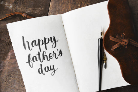 Notebook with 'happy father's day' text on a wooden surface with a pen and leather case.